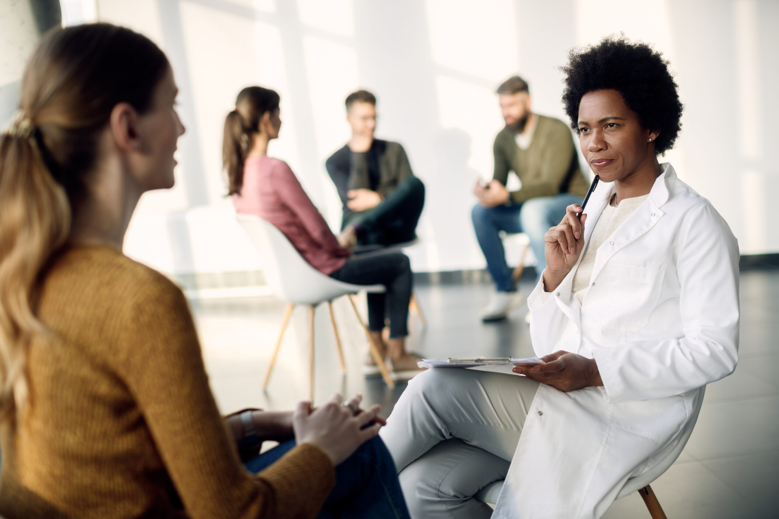 African American psychotherapist talking to female patient during group therapy.